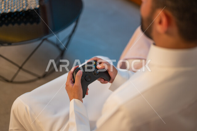 التفاعل والاندماج مع ألعاب الفيديو، زوجان عربيان خليجيان سعوديان يمسكان عصا التحكم بتعابير السرور والسعادة، فعاليات عطلة نهاية الأسبوع، تقنيات الكترونية حديثة ترفيهيه، قضاء وقت ممتع ومسلي في المنزل