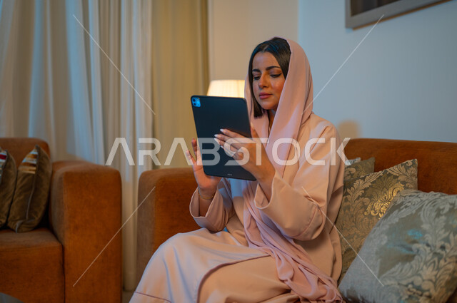 التطبيقات التقنية للأجهزة اللوحية، استخدام الأجهزة والتقنيات الحديثة والمتطورة، إمرأة عربية خليجية سعودية ترتدي العباءة والحجاب تقوم باستخدام الايباد، إنجاز المهام في المنزل، ايماءات الاندماج والتركيز، مهن ووظائف سعودية نسائية، ادارة الأعمال عن بعد
