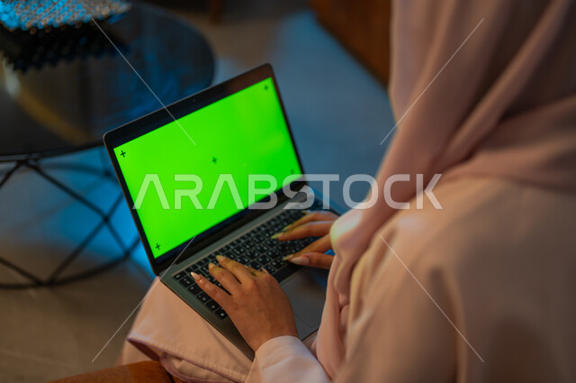 Integrating technology and techniques to follow up and develop business, a close-up photograph from the back of a Saudi Gulf Arab woman typing on a laptop keyboard with a blank green screen, completing tasks at home, Saudi women’s professions and jobs, using modern devices and technologies, chroma