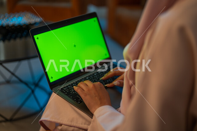 Integrating technology and techniques to follow up and develop business, a close-up photograph from the back of a Saudi Gulf Arab woman typing on a laptop keyboard with a blank green screen, completing tasks at home, Saudi women’s professions and jobs, using modern devices and technologies, chroma