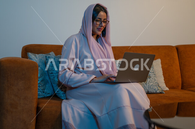 ايماءات التركيز والاندماج، دمج التكنولوجيا بالعمل، مهن ووظائف سعودية نسائية، ادارة الأعمال عن بعد، استخدام الأجهزة والتقنيات الحديثة والمتطورة، إمرأة عربية خليجية سعودية ترتدي العباءة والحجاب تقوم باستخدام الحاسب المحمول، إنجاز المهام في المنزل