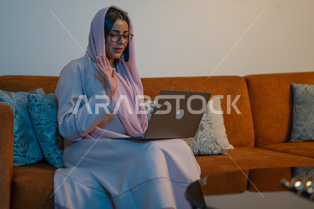 ايماءات التركيز والاندماج، دمج التكنولوجيا بالعمل، مهن ووظائف سعودية نسائية، ادارة الأعمال عن بعد، استخدام الأجهزة والتقنيات الحديثة والمتطورة، إمرأة عربية خليجية سعودية ترتدي العباءة والحجاب تقوم باستخدام الحاسب المحمول، إنجاز المهام في المنزل