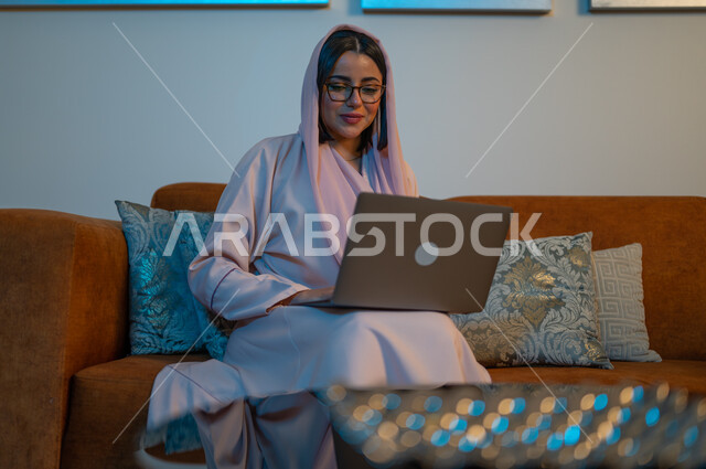 ايماءات التركيز والاندماج، دمج التكنولوجيا بالعمل، مهن ووظائف سعودية نسائية، ادارة الأعمال عن بعد، استخدام الأجهزة والتقنيات الحديثة والمتطورة، إمرأة عربية خليجية سعودية ترتدي العباءة والحجاب تقوم باستخدام الحاسب المحمول، إنجاز المهام في المنزل