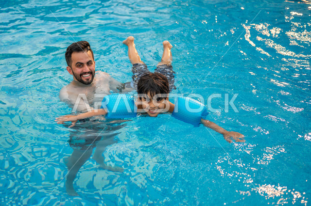 قضاء أوقات ممتعة ومنعشة في فصل الصيف، الرحلات الترفيهيه الممتعة، مفهوم الأسرة السعيدة المترابطة, أب عربي سعودي خليجي يعلم ابنه مهارة السباحة في بركة مائية، الاستمتاع في إحدى مسابح المملكة العربية السعودية، شاليهات ومنتجعات سياحية