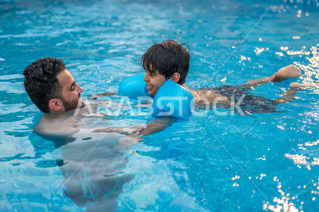 الرحلات الترفيهيه الممتعة، قضاء أوقات ممتعة ومنعشة في فصل الصيف، مفهوم الأسرة السعيدة المترابطة, أب عربي سعودي خليجي يعلم ابنه مهارة السباحة في بركة مائية، الاستمتاع في إحدى مسابح المملكة العربية السعودية، شاليهات ومنتجعات سياحية