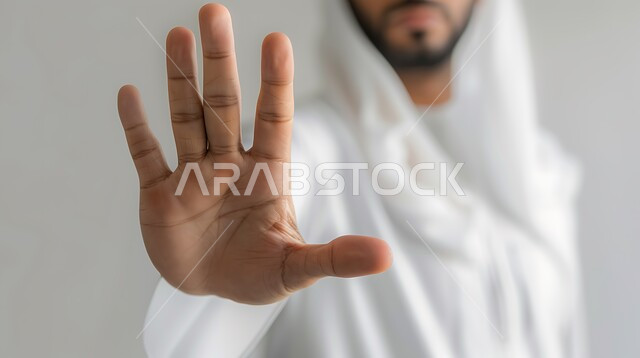 إيماءات الخوف والقلق والانزعاج من أمر ما، طلب التوقف والإمتناع عن فعل شيء ما، بورتريه مقرب لرجل عربي خليجي سعودي يرتدي الشماغ والثوب التقليدي يرفع يده لأعلى بإشارة توقف، عدم القبول ورفض الأذى، خلفية رمادية