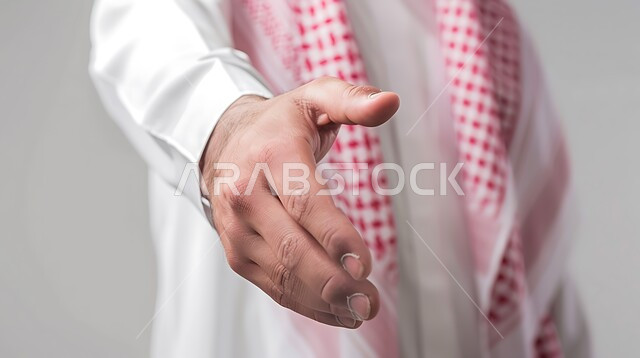 التعارف و الصداقه وتكوين علاقات, إلقاء التحيه والسلام, بورتريه مقرب ليد رجل عربي خليجي سعودي يرتدي الثوب التقليدي والشماغ يقوم بمد كفه للمصافحة, مفهوم الاستقبال والترحيب، خلفية رمادية