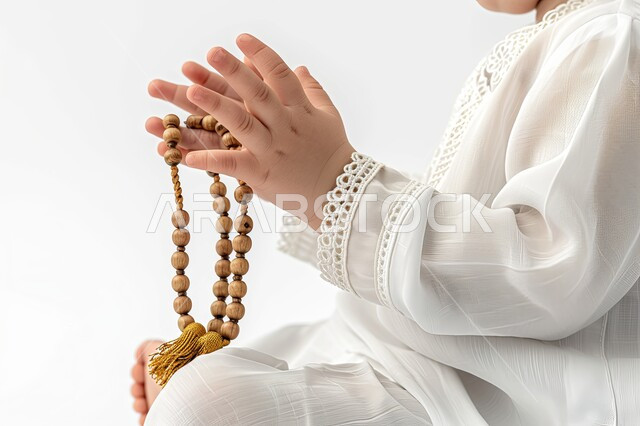 مفهوم الإجتهاد في العباده و التقرب الى الله في شهر رمضان المبارك, الإكثار من ذكر الله تعالى والإستغفار والدعاء, تصوير مقرب لأيدي ولد عربي سعودي خليجي يرتدي الثوب الأبيض يرفع يديه يمسك السبحه, يوم الجمعه المباركه، خلفيه بيضاء