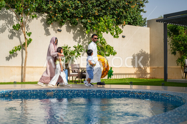 عطلة صيفية وأجواء عائلية سعيدة، قضاء اوقات ممتعة في احد المنتجعات السعودية ، رحلة سياحية ترفيهية، الاستمتاع في إجازة الصيف، عائلة عربية خليجية سعودية تمشي على حدود البركة المائية