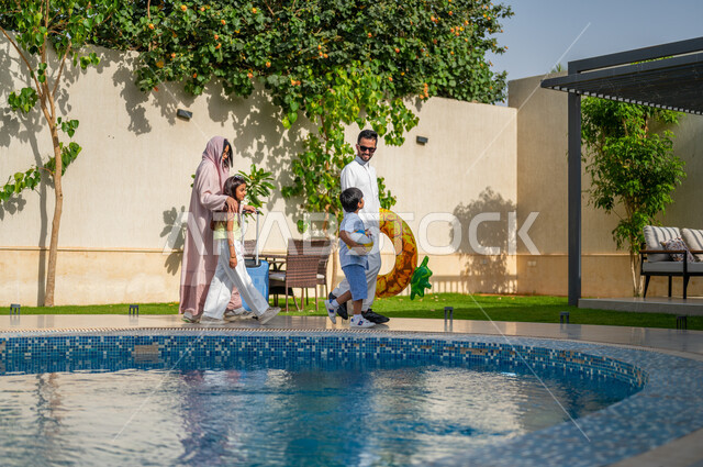 أجواء عائلية سعيدة في العطلة الصيفية، قضاء اوقات ممتعة في احد المنتجعات السعودية ، رحلة سياحية ترفيهية، الاستمتاع في إجازة الصيف، عائلة عربية خليجية سعودية تمشي على حدود البركة المائية