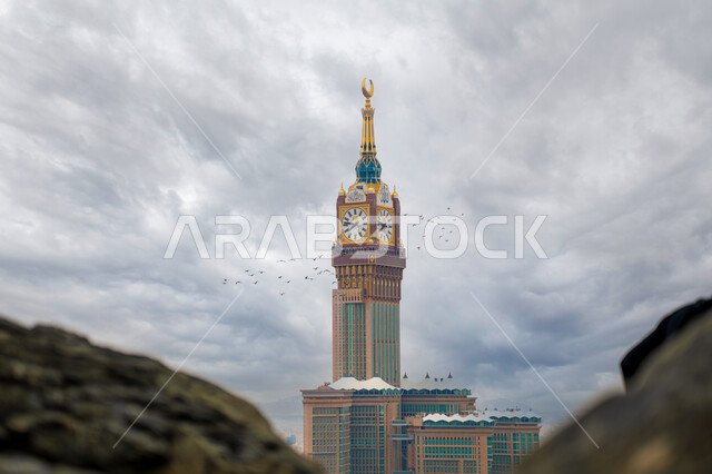 الفن الهندسي المعماري لبرج الساعة المطل على بيت الله الحرام في الحرم المكي الشريف في المملكة العربية السعودية، أماكن ومعالم إسلامية مقدسة، مفهوم العبادة والتقرب الى الله, خلفية السماء الملبدة في الغيوم في وقت النهار