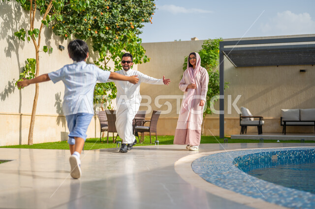 بناء علاقة قوية مع الأولاد، الإجتماع مع العائله وفرحة العوده من السفر، ايماءات تدل على الحماس والسعاده، رجل عربي خليجي سعودي يرتدي الثوب التقليدي يفتح يديه لاحتضان ابنه، دور الأب في حياة الأبناء، قضاء أوقات عائلية ممتعة في المنتجعات السياحية