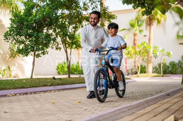 Enjoying family time during the summer vacation, expressions of enthusiasm and pleasure, entertaining recreational activities, a Saudi Gulf Arab boy riding a bike with the help of his father, practicing cycling, upscale resorts and chalets in Saudi Arabia