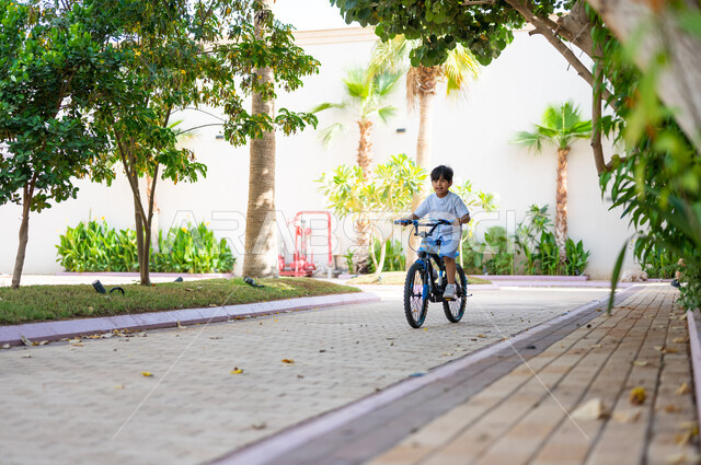Physical activity to maintain physical fitness, practicing the hobby of cycling, a Saudi Gulf Arab boy riding a bike perfectly, spending free time learning fun recreational activities for children, the concept of participating in races.