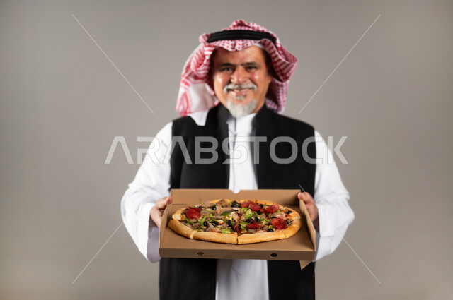 أصناف المعجنات والفطائر الشهية، طلبات الأطعمة الخارجية، بورتريه مقرب لرجل عربي خليجي سعودي كبير بالسن يرتدي الثوب التقليدي والشماغ والستره الوقائيه يحمل البيتزا في علبة كرتون، أضرار تناول وجبات طعام غير صحية، مطاعم المأكولات الغربية في السعودية، خلفية رمادية