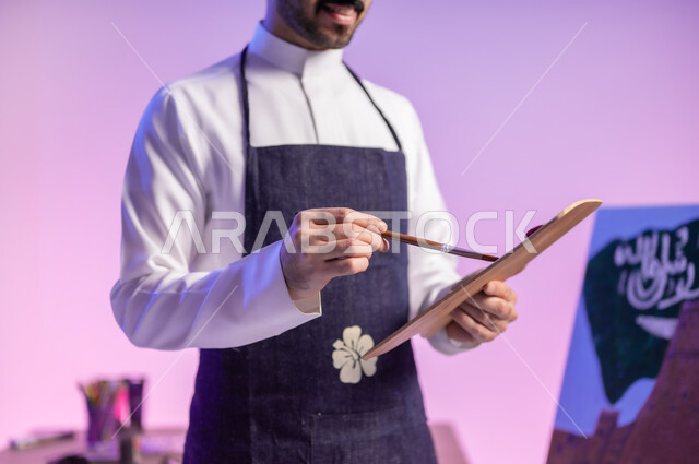 دمج الألوان مع بعضها، استخدام أدوات ومعدات التلوين، الوقوف أمام لوحة معالم وعلم المملكة، بورتريه مقرب لرسام عربي خليجي سعودي يرتدي الثوب التقليدي ومريلة الرسم، إحياء ذكرى اليوم الوطني، ممارسة هواية الرسم والفنون اليدوية، خلفية ملونة