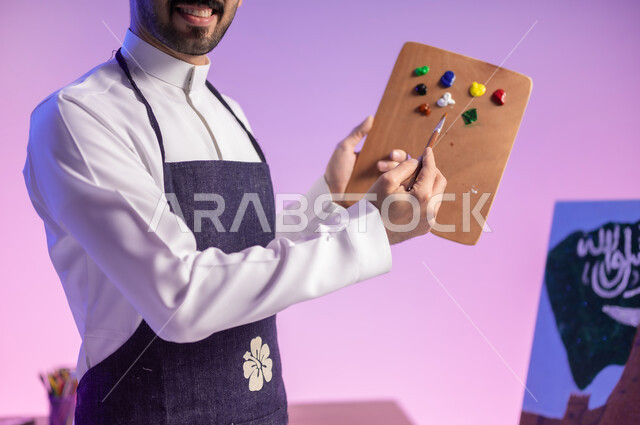 الإشارة الى اللون الأبيض، استخدام أدوات ومعدات التلوين، الوقوف أمام لوحة معالم وعلم المملكة، بورتريه مقرب لرسام عربي خليجي سعودي يرتدي الثوب التقليدي ومريلة الرسم، إحياء ذكرى اليوم الوطني، ممارسة هواية الرسم والفنون اليدوية، خلفية ملونة