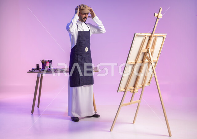 مهارة وهواية الرسم والتلوين، الوقوف أمام اللوحة واضعاً يديه على رأسه بتعابير الانزعاج وعدم الرضا، بورتريه لرسام عربي خليجي سعودي يرتدي الثوب التقليدي ومريلة الرسم، ممارسة الهوايات المفضلة، أنشطة ترفيهية فنية ممتعة، الجسم بالطول الكامل، خلفية ملونة