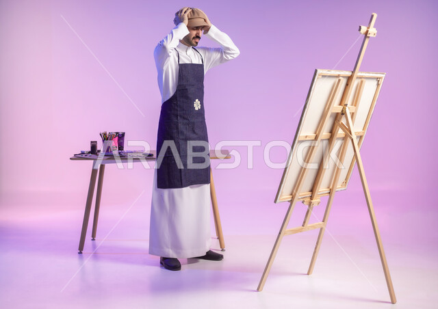 الوقوف أمام اللوحة واضعاً يديه على رأسه بتعابير الانزعاج وعدم الرضا، بورتريه لرسام عربي خليجي سعودي يرتدي الثوب التقليدي ومريلة الرسم، ممارسة الهوايات المفضلة، أنشطة ترفيهية فنية ممتعة، مهارة وهواية الرسم والتلوين، الجسم بالطول الكامل، خلفية ملونة