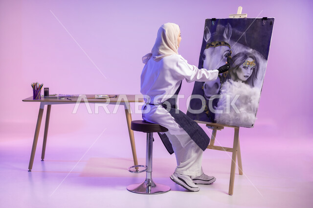 ممارسة مهنة الرسم، استخدام ريشة التلوين والرسم، الجلوس أمام لوحة خيل عربي أصيل أبيض وبجانبه إمرأة، عشق الحصان السعودي الأصيل، بورتريه لرسامة عربية خليجية سعودية ترتدي اللباس الكاجوال ومريلة الرسم، الجسم بالطول الكامل، خلفية ملونة