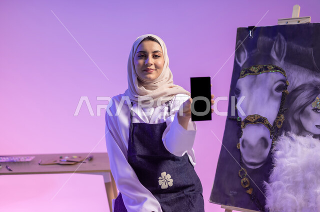Using modern technologies, loving the purebred Saudi horse, sitting in front of a painting of a purebred white Arabian horse with a woman next to him, a close-up portrait of a Saudi Arabian Gulf painter wearing casual clothes and a drawing apron, looking at the camera with a happy gesture, a blank black screen, a colored background.