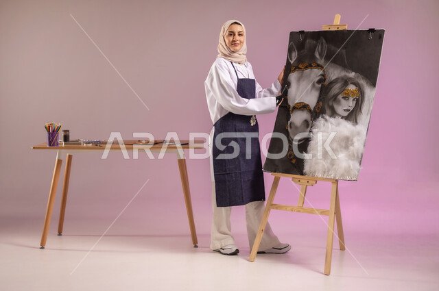 استخدام ريشة التلوين والرسم، عشق الحصان السعودي الأصيل، الوقوف أمام لوحة خيل عربي أصيل أبيض وبجانبه إمرأة، بورتريه  لرسامة عربية خليجية سعودية ترتدي اللباس الكاجوال ومريلة الرسم، النظر للكاميرا بإيماءا السعادة، الجسم بالطول الكامل، خلفية ملونة