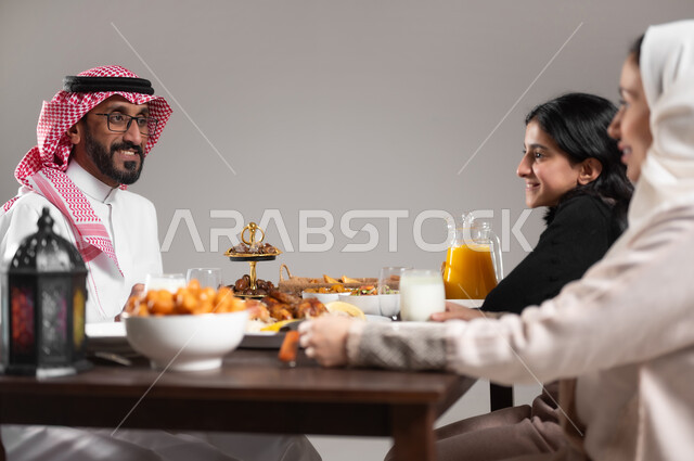 مشاركة العائلة الاجواء السعيدة على مائدة الطعام, بورتريه مقرب لعائلة عربية خليجية سعودية مجتمعة على طاولة الطعام تتبادل الاحاديث, المقبلات و الاصناف الشرقية اللذيذة, ايماءات السعادة و السرور, خلفية رمادية