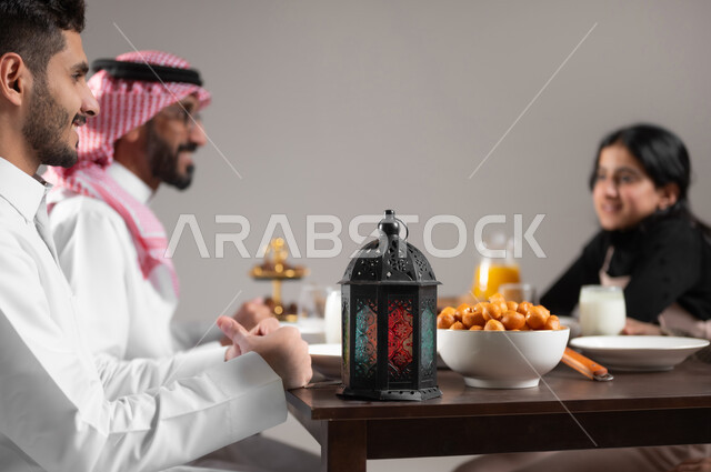 مشاركة العائلة الاجواء السعيدة على مائدة الطعام, بورتريه مقرب لعائلة عربية خليجية سعودية مجتمعة على طاولة الطعام منتظرة اذان المغرب, المقبلات و الاصناف الشرقية اللذيذة, ايماءات السعادة و السرور, خلفية رمادية