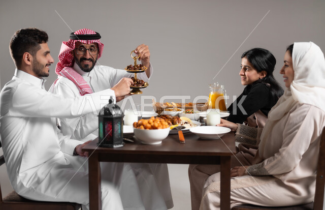 عزومات الاصدقاء على افطار رمضان, بورتريه لعائلة عربية خليجية سعودية مجتمعة على طاولة الطعام, توزيع التمر السعودي على المائدة, المقبلات و الاصناف الشرقية اللذيذة, ايماءات السعادة و السرور