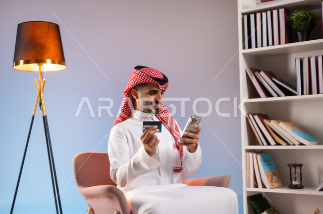 تصفح تطبيقات المصارف والبنوك عبر الهاتف المحمول، الشراء والدفع عبر الاونلاين, استخدام بطاقة الإئتمان في التسوق الالكتروني, بورتريه لرجل عربي خليجي سعودي يرتدي الثوب التقليدي والشماغ يجلس على كرسي ويمسك البطاقة البنكية, خلفية ملونة