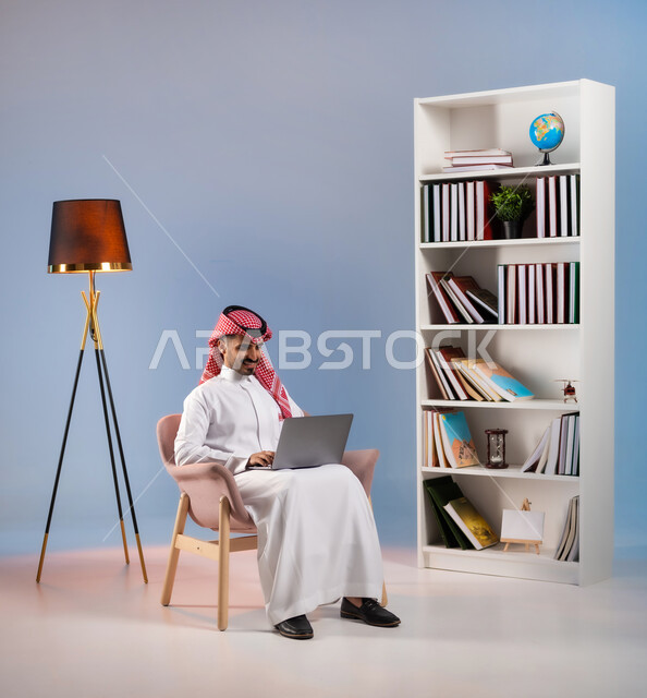 إدراة الأعمال عن بعد, انجاز المهام عبر الانترنت, التسوق الالكتروني والشراء عبر التطبيقات والتقنيات الحديثة, بورتريه لرجل عربي خليجي سعودي يرتدي الثوب التقليدي والشماغ يعمل على الحاسب المحمول, استخدام الأجهزة المتطورة في المملكة, خلفية ملونة