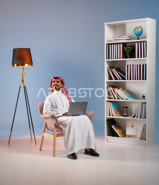 تصفح مواقع التواصل الاجتماعي, النظر إلى شيء ما بإيماءات التمعن والتركيز, بورتريه لرجل عربي خليجي سعودي يرتدي الثوب التقليدي والشماغ يعمل على الحاسب المحمول, استخدام الأجهزة والتقنيات الحديثة والمتطورة, خلفية ملونة