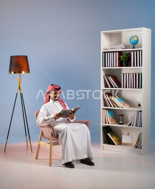 قضاء أوقات الفراغ بممارسة هواية المطالعة, مفهوم الثقافة والتعلم الذاتي, قراءة القصص والروايات الممتعة, بورتريه لرجل عربي خليجي سعودي يرتدي الثوب التقليدي والشماغ يجلس على الكرسي ويمسك بيده كتاب, تنمية الذخيرة الثقافية, خلفية ملونة