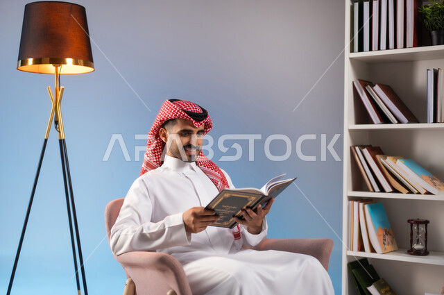 مفهوم الثقافة والتعلم الذاتي, قراءة القصص والروايات الممتعة, بورتريه لرجل عربي خليجي سعودي يرتدي الثوب التقليدي والشماغ يجلس على الكرسي ويمسك بيده كتاب, تنمية الذخيرة الثقافية, قضاء أوقات الفراغ بممارسة هواية المطالعة, خلفية ملونة