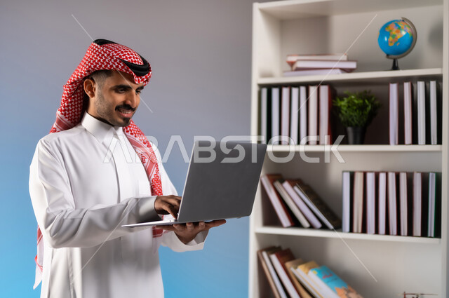 الدردشة والمحادثة مع الأصدقاء عبر السوشال ميديا, تصفح مواقع التواصل الاجتماعي, بورتريه مقرب لرجل عربي خليجي سعودي مبتسم يرتدي الثوب التقليدي والشماغ يعمل على الحاسب المحمول, إدراة وانجاز المهام عبر الانترنت, خلفية ملونة