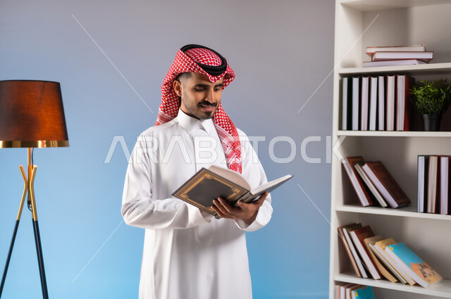 مفهوم الثقافة والتعلم الذاتي, قراءة القصص والروايات الممتعة, بورتريه لرجل عربي خليجي سعودي يرتدي الثوب التقليدي والشماغ يمسك بيده كتاب, تنمية الذخيرة الثقافية, قضاء أوقات الفراغ بممارسة هواية المطالعة, خلفية ملونة