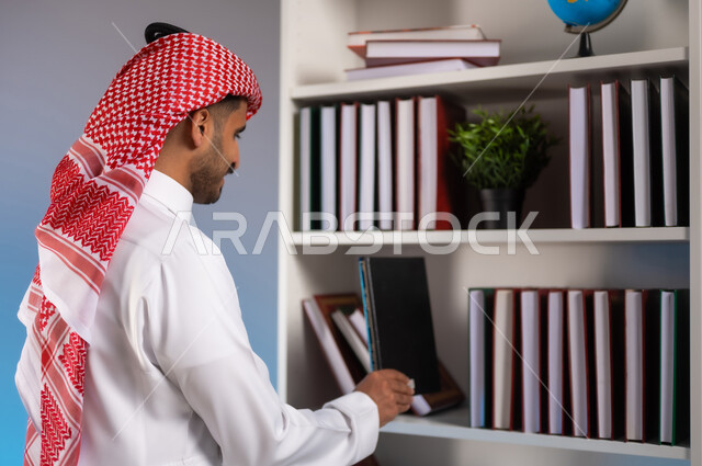 محبي وهواة المطالعة في المملكة, مفهوم القراءة والثقافة, تنمية الذخيرة العلمية, الاستمتاع بممارسة الهوايات المفيدة, بورتريه مقرب من الجانب لرجل عربي خليجي سعودي يرتدي الثوب التقليدي والشماغ يقوم باقتناء الكتاب من المكتبة, خلفية ملونة