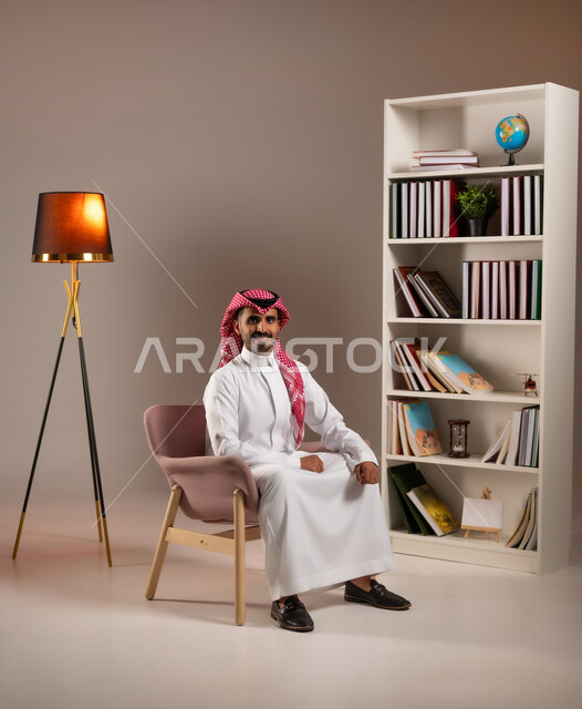 Elegance, elegance, and attention to external appearance, a portrait of a smiling Saudi Arabian Gulf man wearing the traditional dress and shemagh, looking at the camera with gestures of self-confidence, the concept of handsomeness and masculinity, beige background
