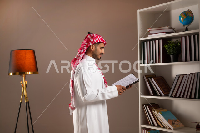 ممارسة الهوايات الممتعة والمفيدة في وقت الفراغ, قراءة الكتب التعليمية التثقيفة, بورتريه من الجانب لرجل عربي خليجي سعودي يرتدي الثوب التقليدي والشماغ يمسك بيده الكتاب, مفهوم التعلم الذاتي, اتباع أسلوب حياة صحي, اقتناء واختيار الكتب من المكتبة المنزلية. خلفية بيج