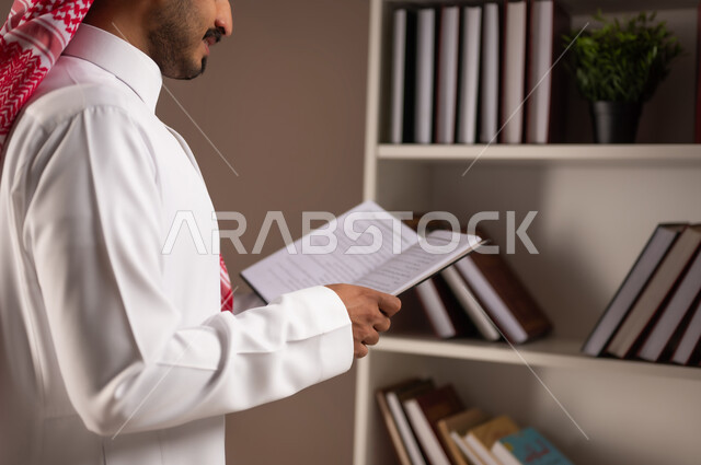 قراءة الكتب التعليمية التثقيفة, بورتريه مقرب من الجانب لرجل عربي خليجي سعودي يرتدي الثوب التقليدي والشماغ يمسك بيده الكتاب, مفهوم التعليم الذاتي, اتباع أسلوب حياة صحي, ممارسة الهوايات الممتعة والمفيدة في وقت الفراغ, خلفية بيج