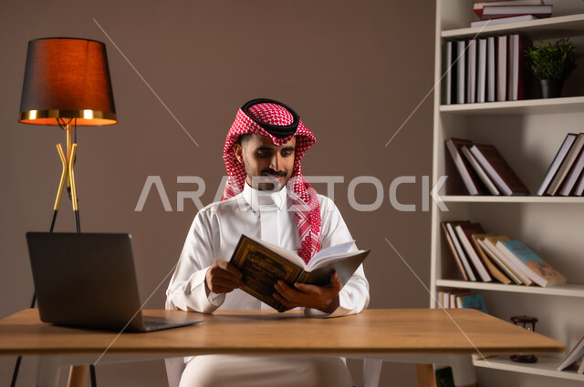 The concept of culture and self-learning, enjoying useful recreational activities in free time, practicing the hobby of reading, reading stories and novels, a portrait of a Saudi Gulf Arab man wearing the traditional dress and shemagh, holding a book in his hand, using modern electronic devices and applications, beige background