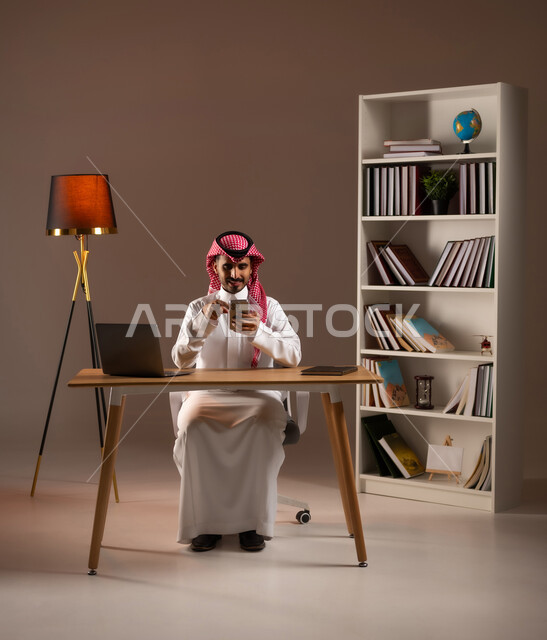 Browsing the Internet and using modern technologies, chatting and conversing with family and friends, following social media news, a portrait of a Saudi Gulf Arab man wearing a traditional thobe and shemagh, using a mobile phone, making a video call via mobile phone, beige background