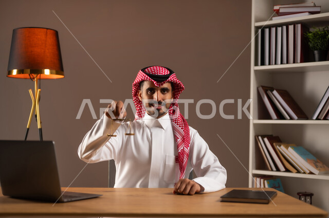 العمل في مجال القضاء والمحاماة, استلام قضية جديدة بتعابير الثقة, مهن ووظائف قانونية, مفهوم العدالة ودراسة القانون, بورتريه مقرب لرجل عربي خليجي سعودي يرتدي الثوب التقليدي والشماغ يمسك ميزان العدل, استخدام الأجهزة والتقنيات الحديثة في المجال القانوني, خلفية بيج