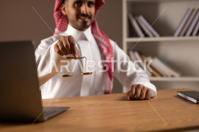 استلام قضية جديدة بتعابير الثقة, العمل في مجال القضاء والمحاماة, مهن ووظائف قانونية, مفهوم العدالة ودراسة القانون, بورتريه مقرب لرجل عربي خليجي سعودي يرتدي الثوب التقليدي والشماغ يمسك ميزان العدل, استخدام الأجهزة والتقنيات الحديثة في المجال القانوني, خلفية بيج