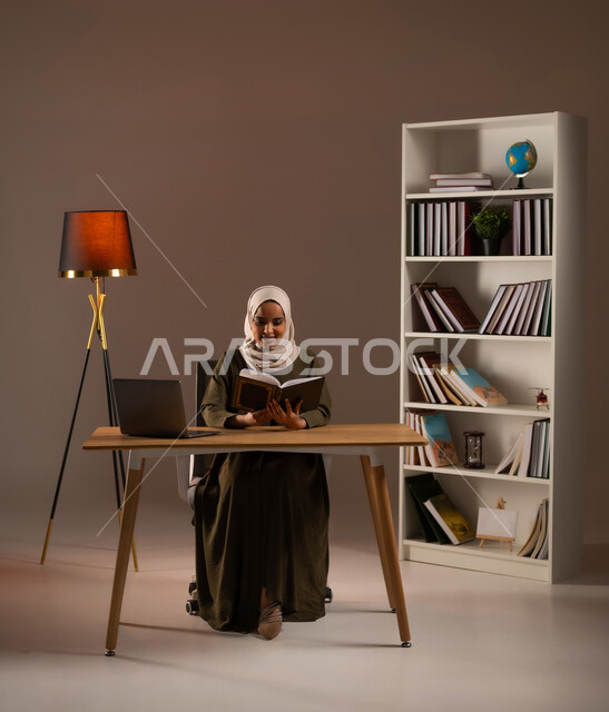 الاستمتاع بقراءة الكتب والقصص والروايات, ثقافة التعلم الذاتي, إنجاز الواجبات اليومية, قضاء الوقت بالقراءة والتعلم والتثقف، بورتريه لامرأة عربية سعودية خليجية محجبة ترتدي العباءة تحمل بيديها كتاب، استخدام الأجهزة والتطبيقات الالكترونية الحديثة, خلفية بيج