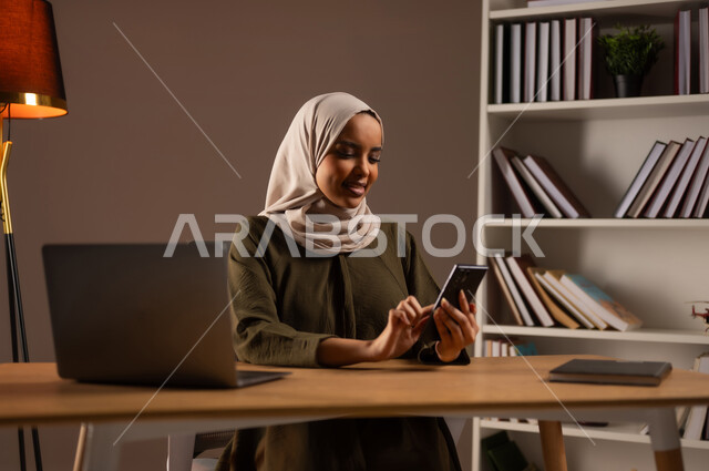 الدردشة والمحادثة مع الأهل والاصدقاء, إجراء مكالمة فيديو عبر الجوال, تصفح الانترنت واستخدام تقنيات حديثة, متابعة أخبار وسائل التواصل الاجتماعي, بورتريه لإمرأة عربية خليجية سعودية مبتسمة ترتدي العباءة تستخدم الهاتف المحمول, خلفية بيج