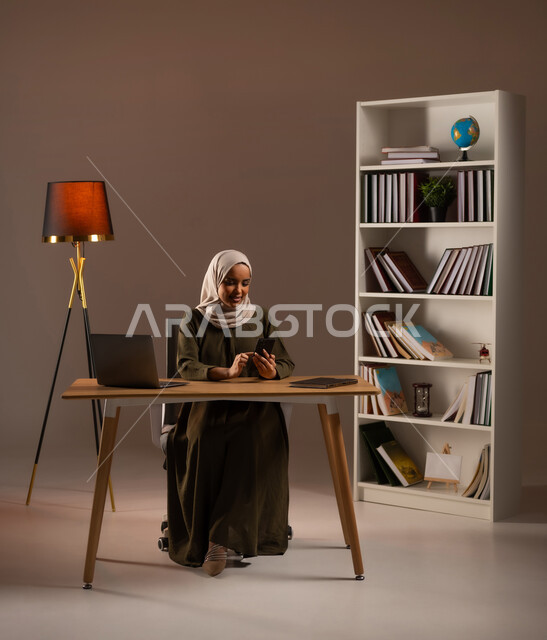 تصفح الانترنت واستخدام تقنيات حديثة, الدردشة والمحادثة مع الأهل والاصدقاء, متابعة أخبار وسائل التواصل الاجتماعي, بورتريه لإمرأة عربية خليجية سعودية ترتدي العباءة تستخدم الهاتف المحمول, إجراء مكالمة فيديو عبر الجوال, خلفية بيج