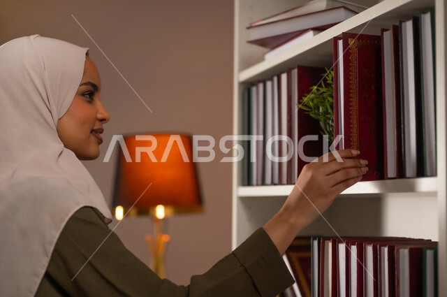 مفهوم القراءة والتثقيف الذاتي والتعلم, بورتريه مقرب من الجانب لشابة عربية خليجية سعودية ترتدي العباءة تقوم باقتناء كتاب من المكتبة, كتب الروايات والقصص, الاستمتاع بممارسة الهوايات المفيدة, اتباع عادات وأسلوب حياة صحي, خلفية بيج