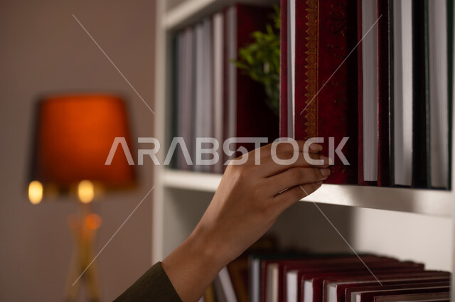 مفهوم القراءة والتثقيف الذاتي والتعلم, بورتريه مقرب ليد شابة عربية خليجية سعودية ترتدي العباءة تقوم باقتناء كتاب من المكتبة, كتب الروايات والقصص, الاستمتاع بممارسة الهوايات المفيدة, اتباع عادات وأسلوب حياة صحي, خلفية بيج