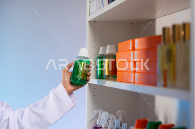 Local national products, work in the Saudi medical sector, the concept of pharmacy and medical supplies, women’s professions and jobs in the Kingdom, a close-up portrait from the side of the hand of a Saudi Arabian Gulf female pharmaceutical doctor wearing a medical uniform holding a medicine package in her hand, colored background